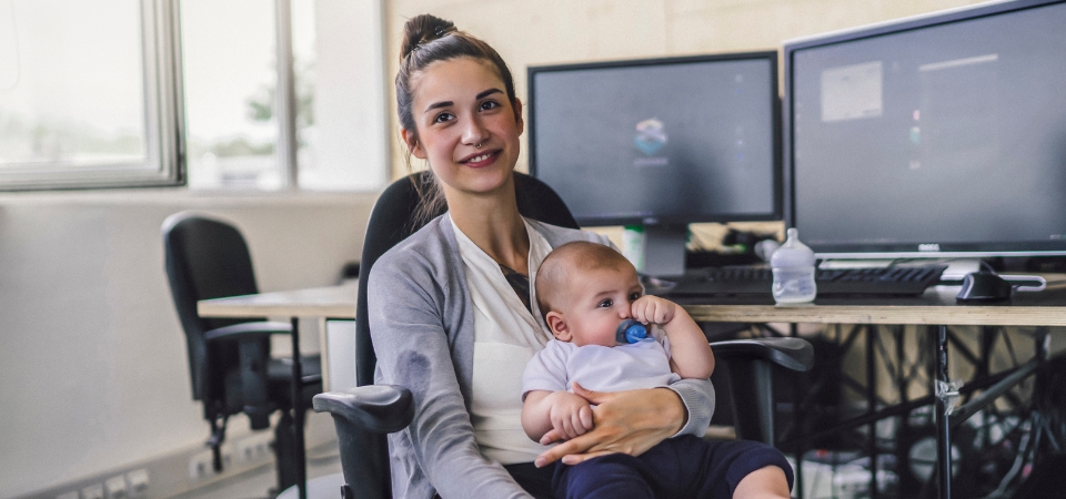 A woman with a baby on her lap poses for a photo in an office.