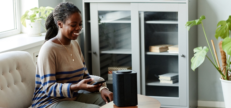 Portrait of smiling African American woman using voice activated smart speaker in cozy home interior, copy space