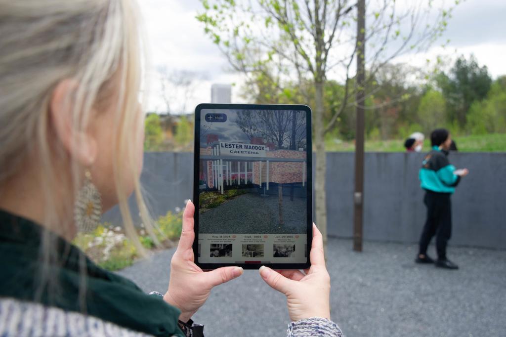 Image showing a woman holding an ipad with the AR aspect of the pickrick project displayed on it. The ipad shows what the location on GT's campus looked like during the pickrick protests. 