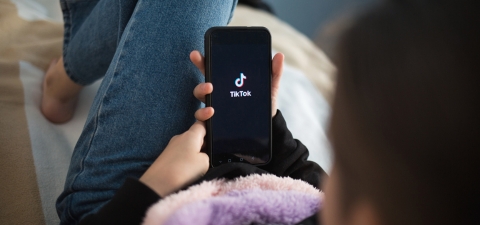 child with phone in his hands is lying at home on bed. Social Media tiktok is loaded on screen