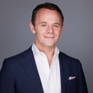 Michael Morley poses, smiling, against a grey background.