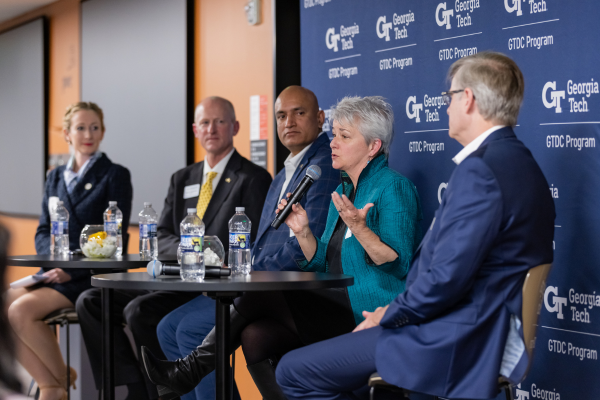 Panelist Ellen Bassett speaks into a microphone while fellow panelists Richard Utz, Devesh Ranjan, Cassidy Sugimoto, and Dene Sheheane look on attentively