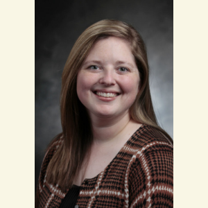 Caroline McWhorter poses, smiling, in front of a grey background.