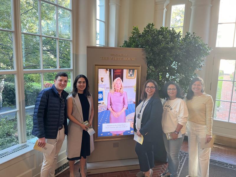 A group of Georgia Tech visitors to Washington, D.C. are gathered around a kiosk picturing Dr. Jill Biden saying "Welcome to the White House."