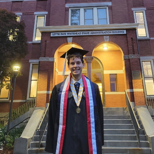 Clashman's grad photo in cap and gown in front of Tech Tower