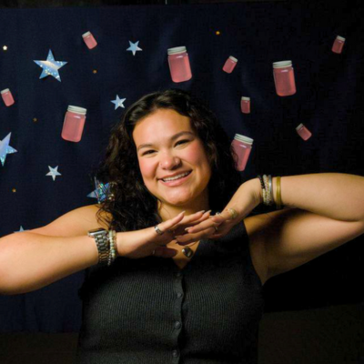 Angela Wrigley poses in front of a background with stars and jam jars from the production Orbital Debris.