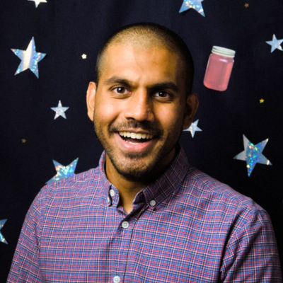 Shrey Patel smiles in front of a decorative background of stars and jars of jam from the production Orbital Debris.