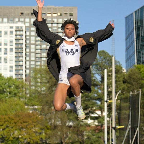Ameia doing the long jump in her track uniform and graduation gown
