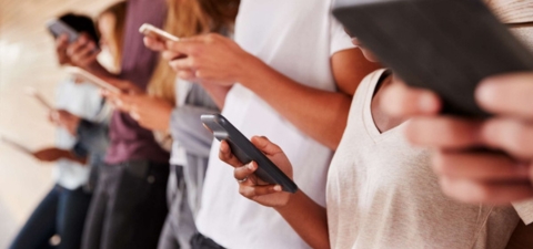 Group of people standing against a wall holding cell phones in their hands.