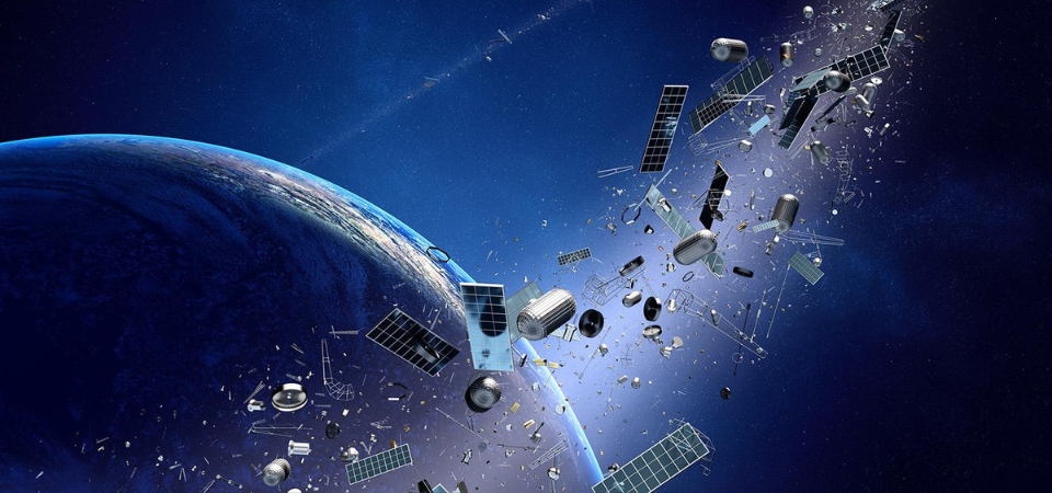 A view of Earth from space with a large amount of space debris orbiting the planet. The debris includes various pieces of satellites, solar panels, and other fragments scattered in a trail extending away from Earth. The background shows the vast expanse of outer space with stars visible in the distance.