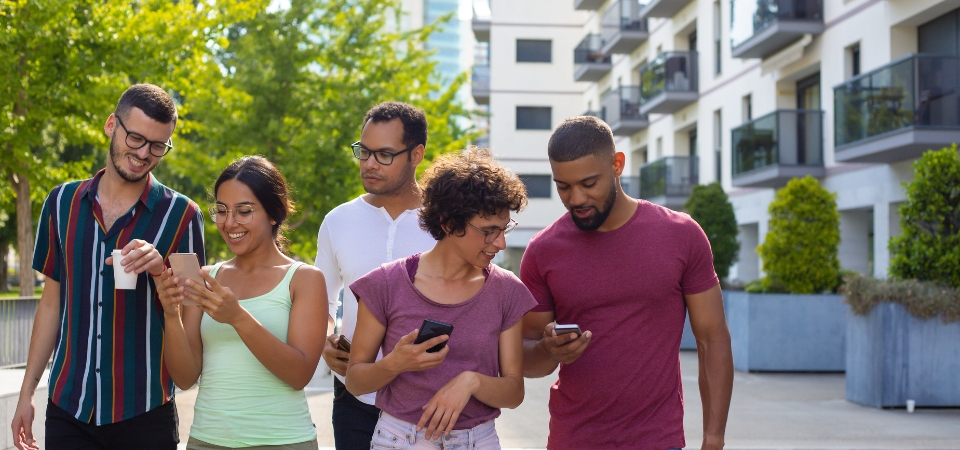 People walking down a sidewalk using cell phones and smiling. 