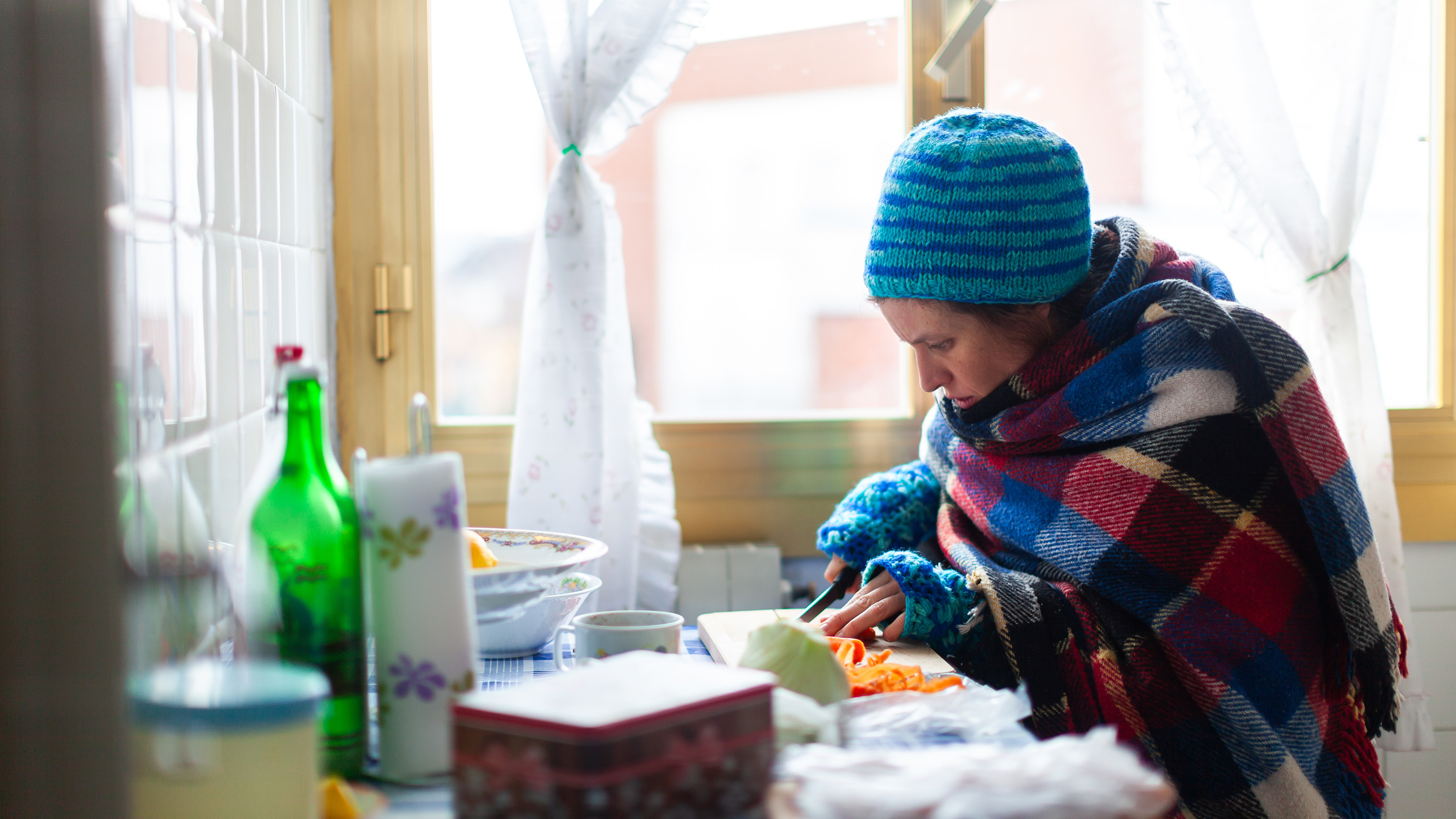 Person dressed in warm clothing inside cutting food.
