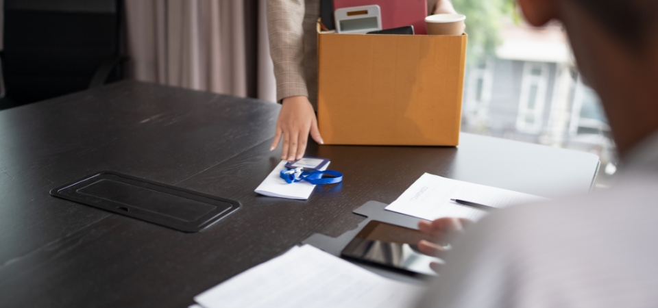 Person holding a box of their belongings at a work table indicating they are leaving their job.