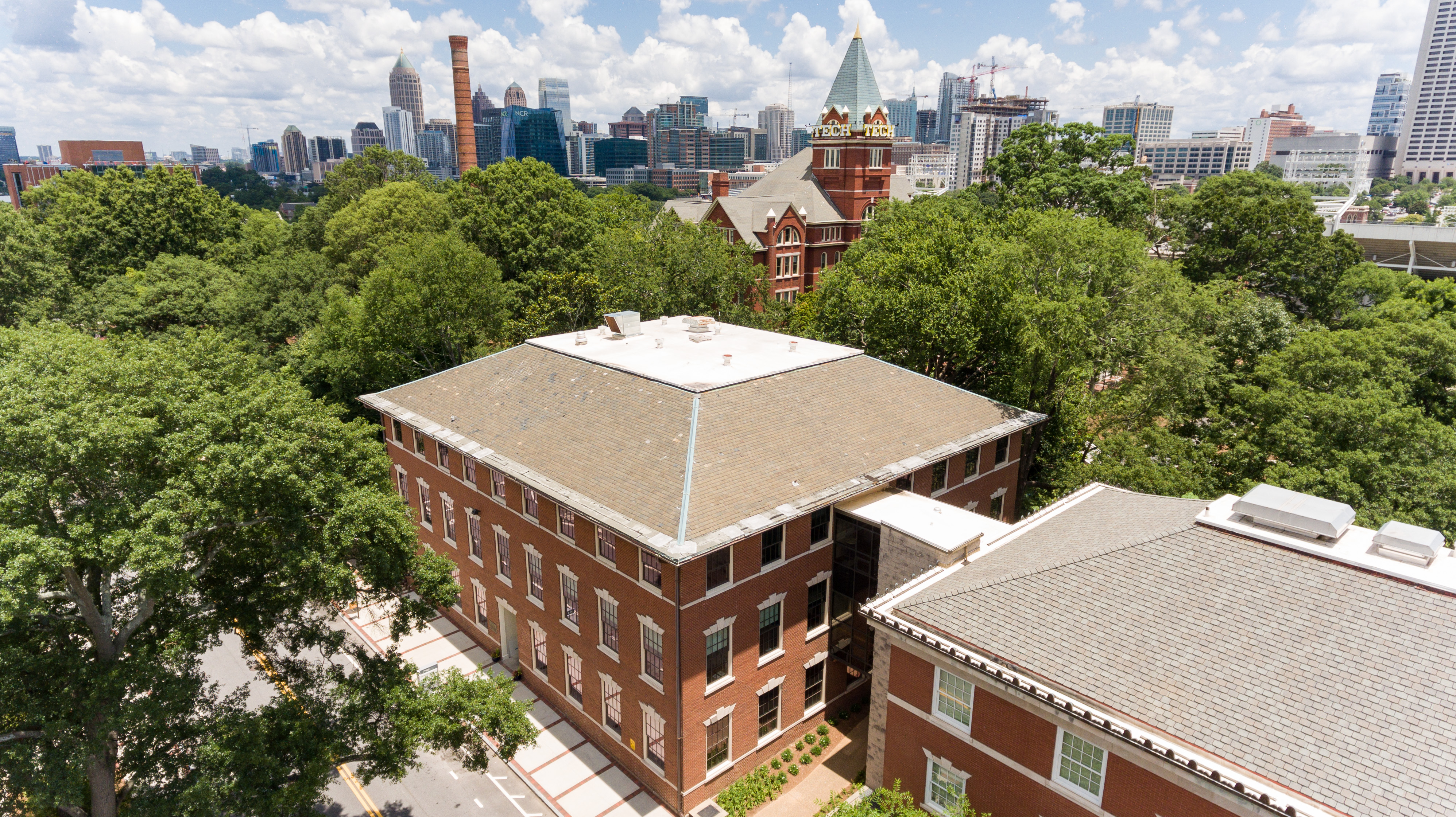 Aerial view of the Savant and Swann Buildings with lush green trees around them. Tech Tower stands tall behind them with the Atlanta skyline in the distance.