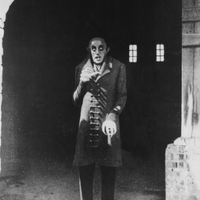 a tall, thin, pale man wearing a long coat and outfitted with pointy ears and fangs