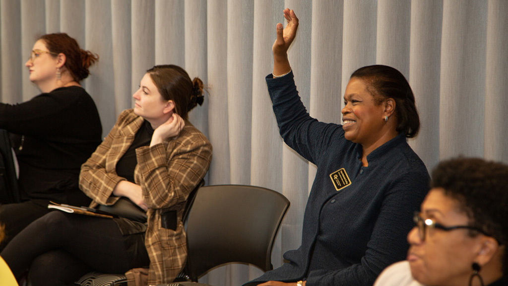 A woman raising her hand to ask a question during a symposium