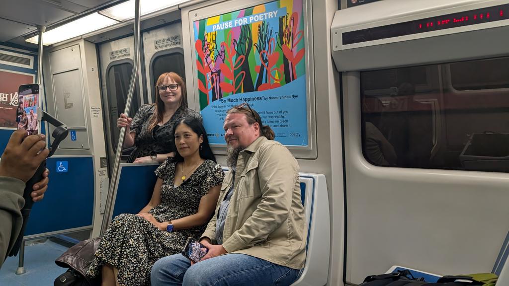 People riding a subway train with a colorful sign in the background