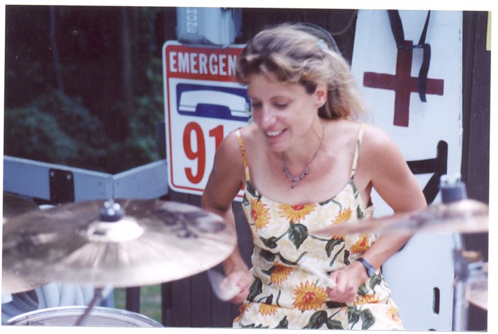 Photo of Kristie Macrakis playing drums wearing a sunflower dress.