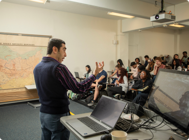 View from behind of history professor lecturing in class with students in front of him engaged in the discussion.
